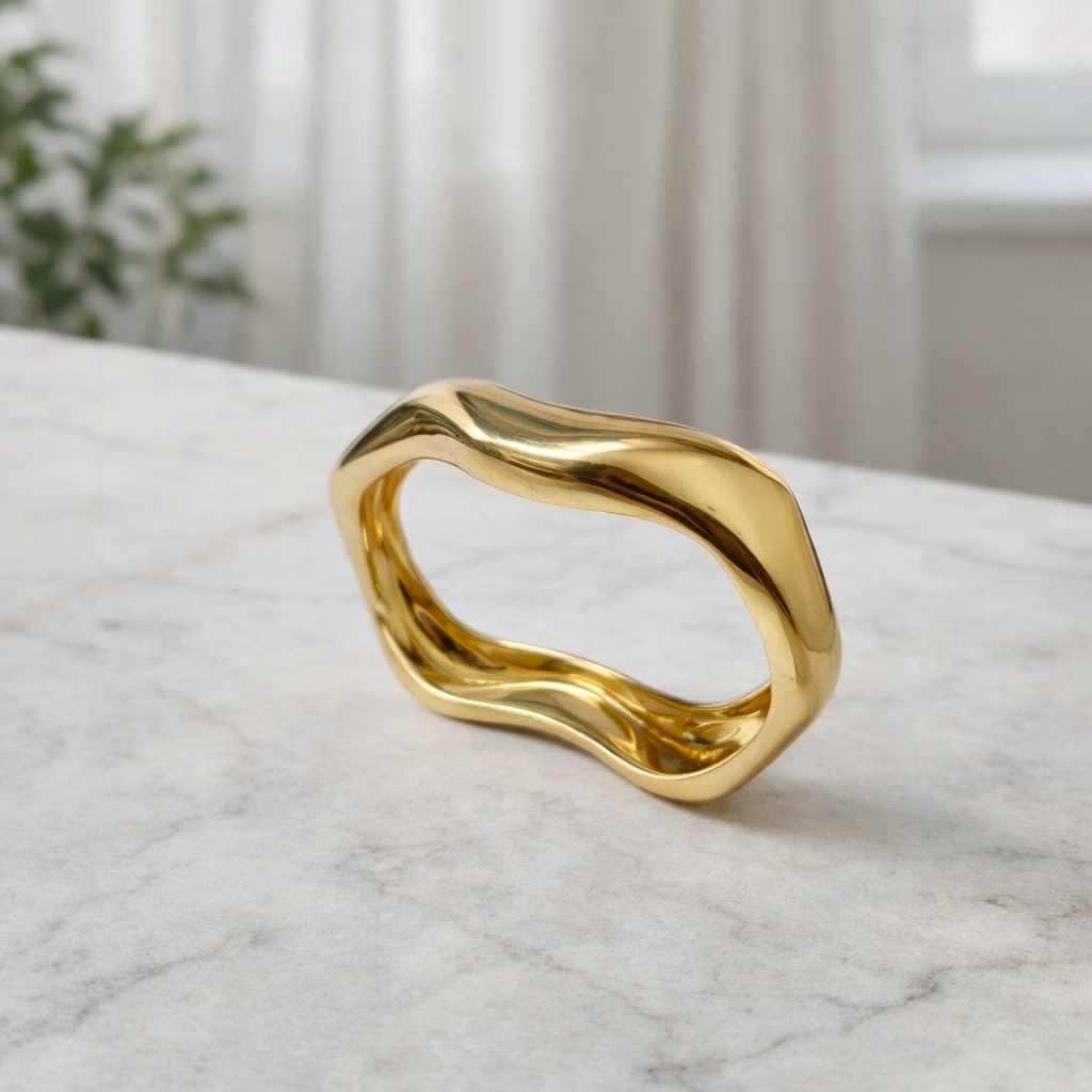 a sleek gold bangle designed with smooth flowing curves on a white counter top.
