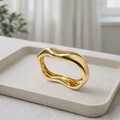 a sleek gold bangle designed with smooth flowing curves on a white plate.