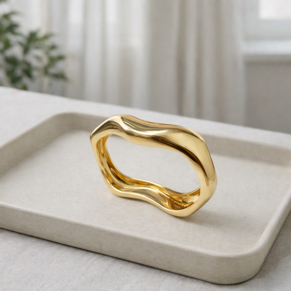 a sleek gold bangle designed with smooth flowing curves on a white plate.