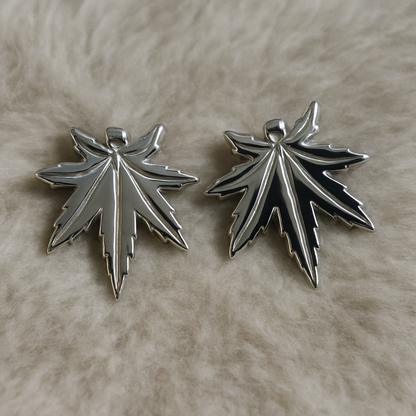 Two silver leaf-shaped pendants on a beige surface