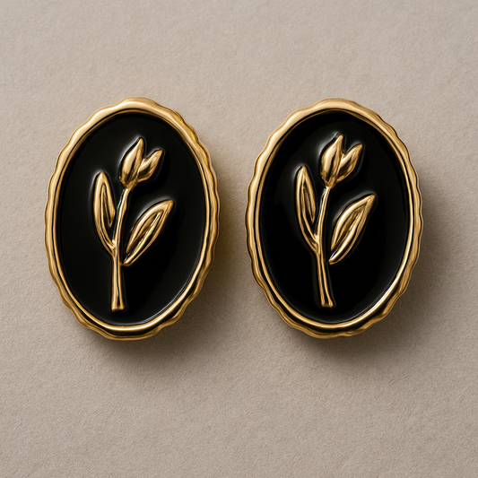 Elegant oval black and gold stud earrings with a raised botanical design on a glossy enamel finish