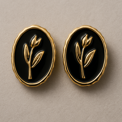 Elegant oval black and gold stud earrings with a raised botanical design on a glossy enamel finish