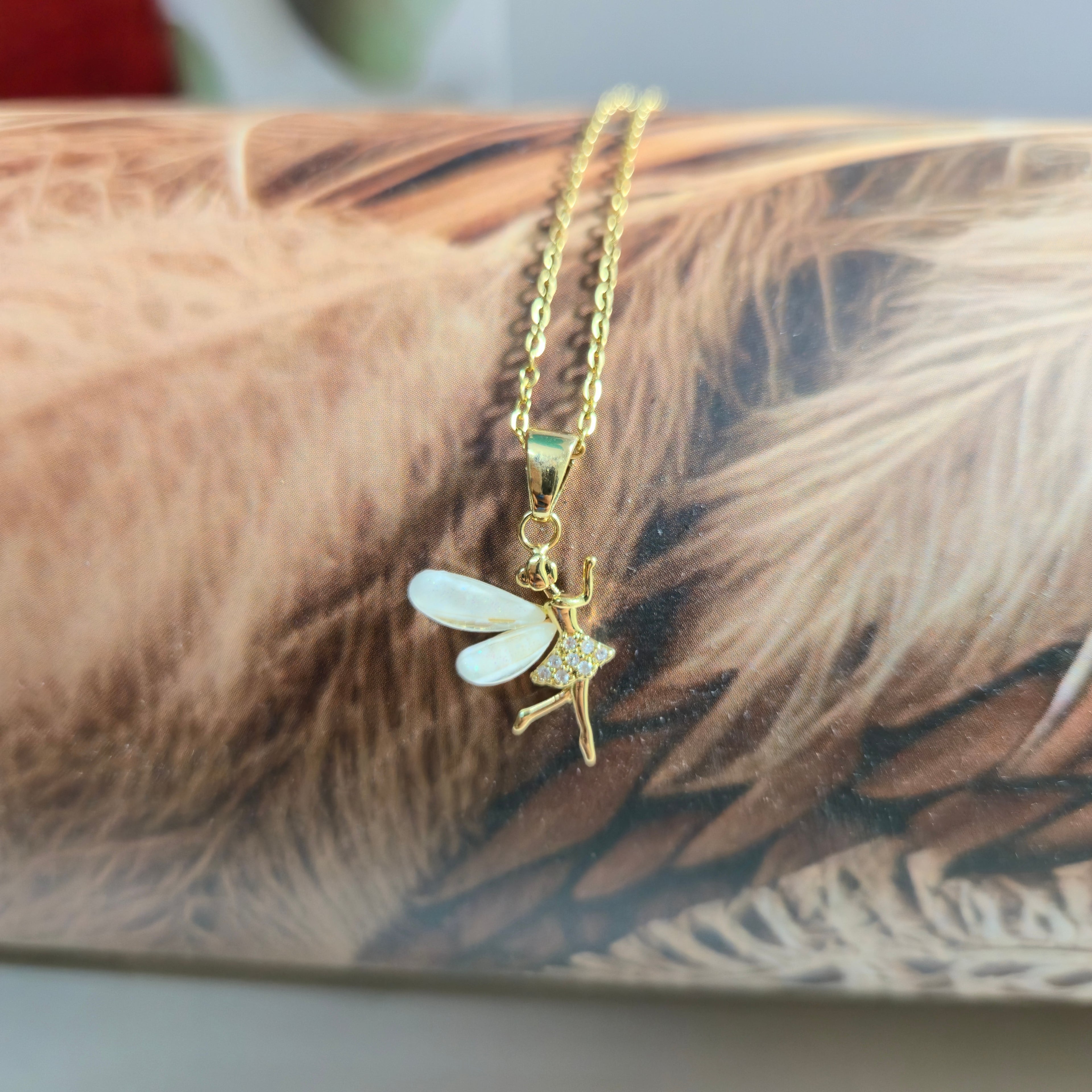 Gold fairy pendant necklace on a feather background