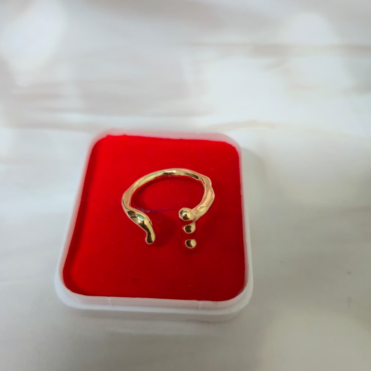 Modern adjustable gold ring with fluid curves displayed in a red velvet jewelry box.
