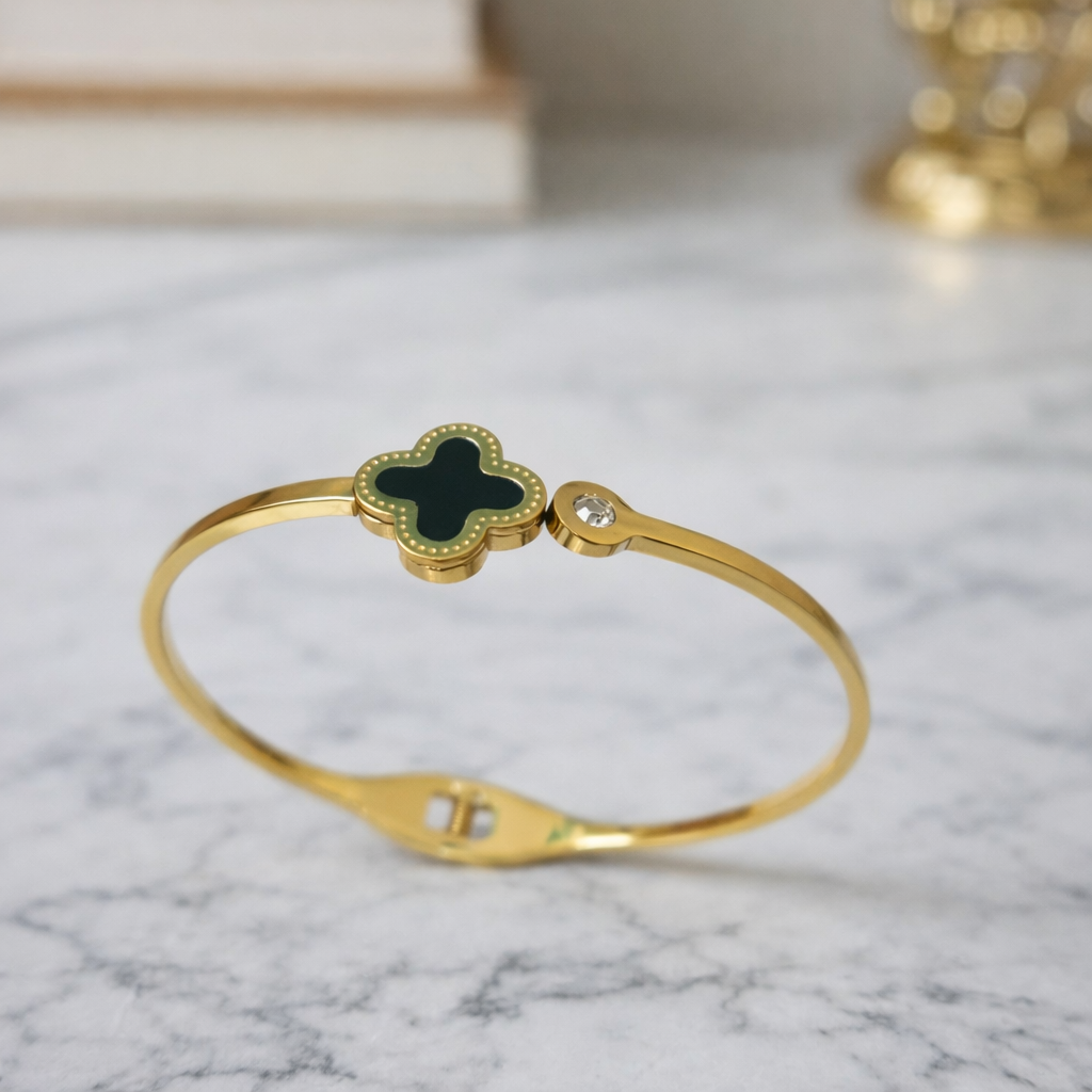 a timeless gold bangle with a rich black clover charm and a subtle sparkling stone on a marble background.
