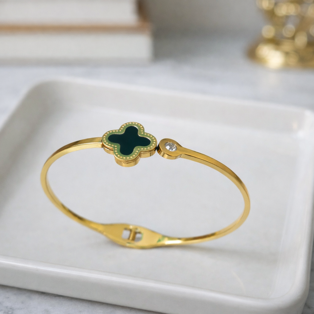 a timeless gold bangle with a rich black clover charm and a subtle sparkling stone on a white plate.