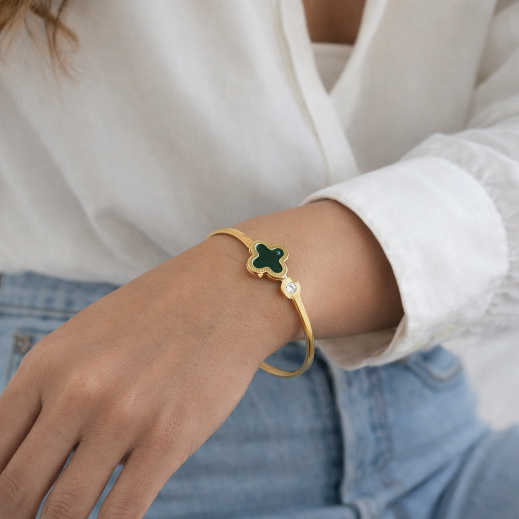 a timeless gold bangle with a rich black clover charm and a subtle sparkling stone on the arm of a woman.