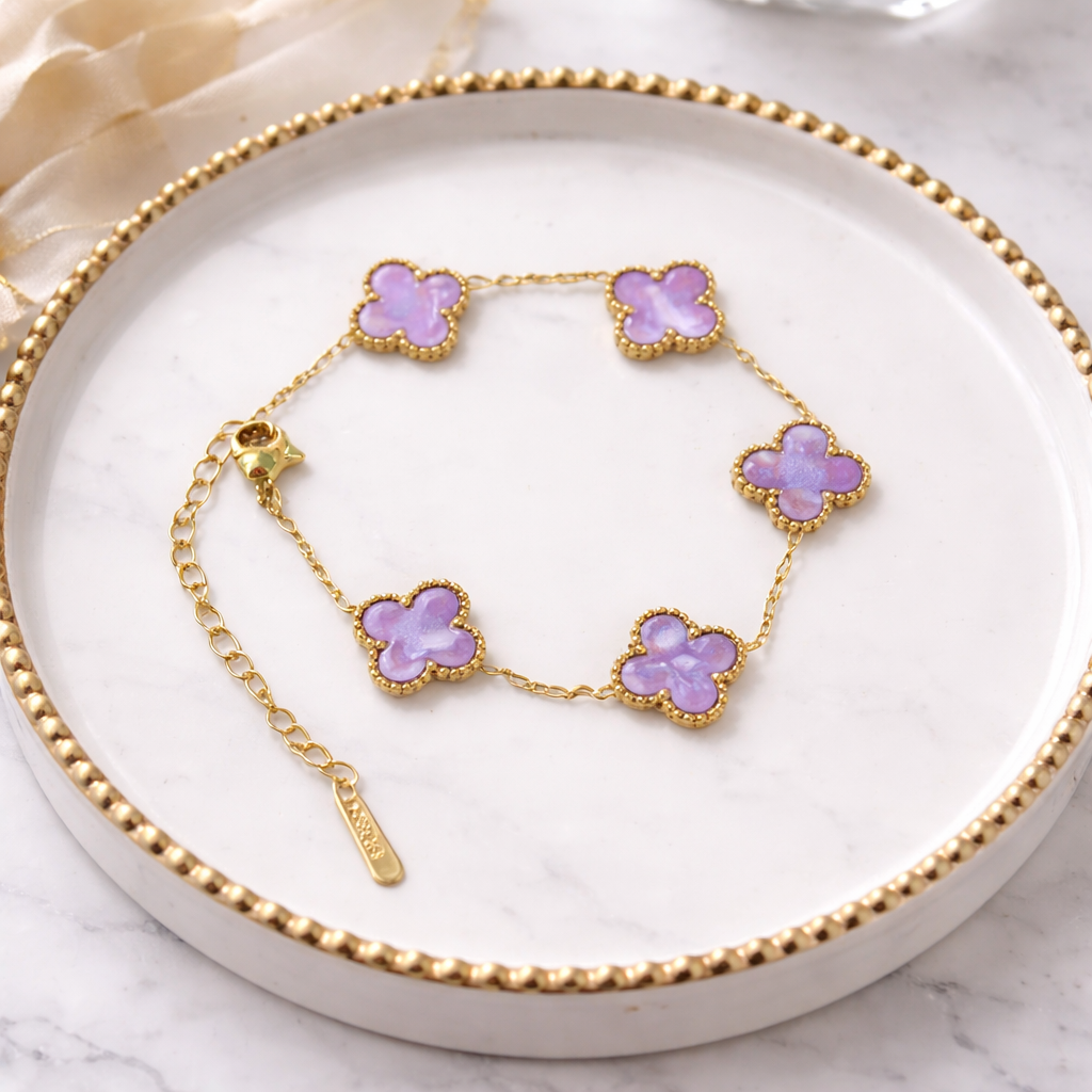 A timeless bracelet crafted in a delicate gold-tone finish, adorned with dreamy lilac clover charms on a white marble plate.