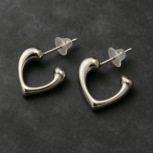 Pair of silver-toned open-heart stud earrings with a polished finish and transparent backings, displayed on a dark textured background.