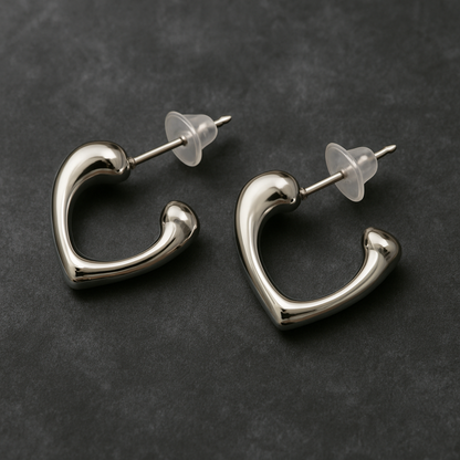 Pair of silver-toned open-heart stud earrings with a polished finish and transparent backings, displayed on a dark textured background.