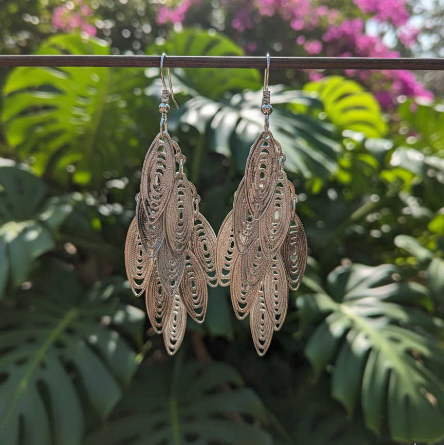 Decorative earrings hanging on a branch with green leaves and pink flowers in the background