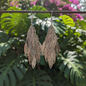Decorative earrings hanging on a branch with green leaves and pink flowers in the background