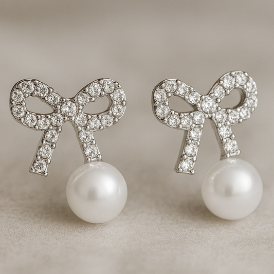 A pair of elegant stud earrings featuring crystal-studded bow designs with dangling white pearls.
