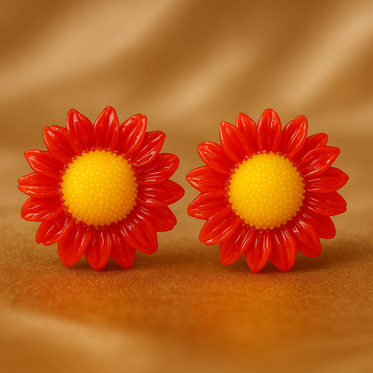 Pair of sunflower-shaped stud earrings with vibrant red petals and bright yellow centers, displayed on a luxurious champagne-colored satin background.
