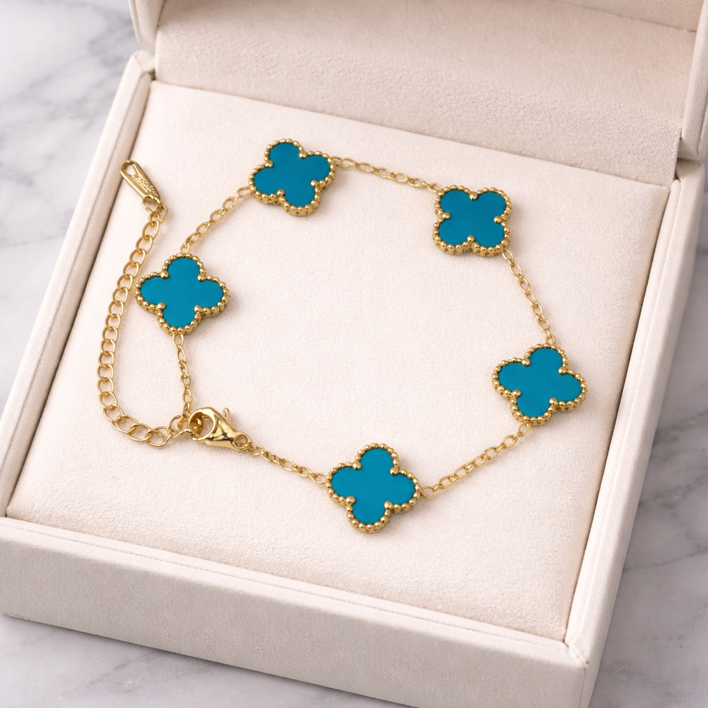 gold-tone clover charm bracelet, featuring turquoise clover stations framed in a delicate beaded border on a white box. 