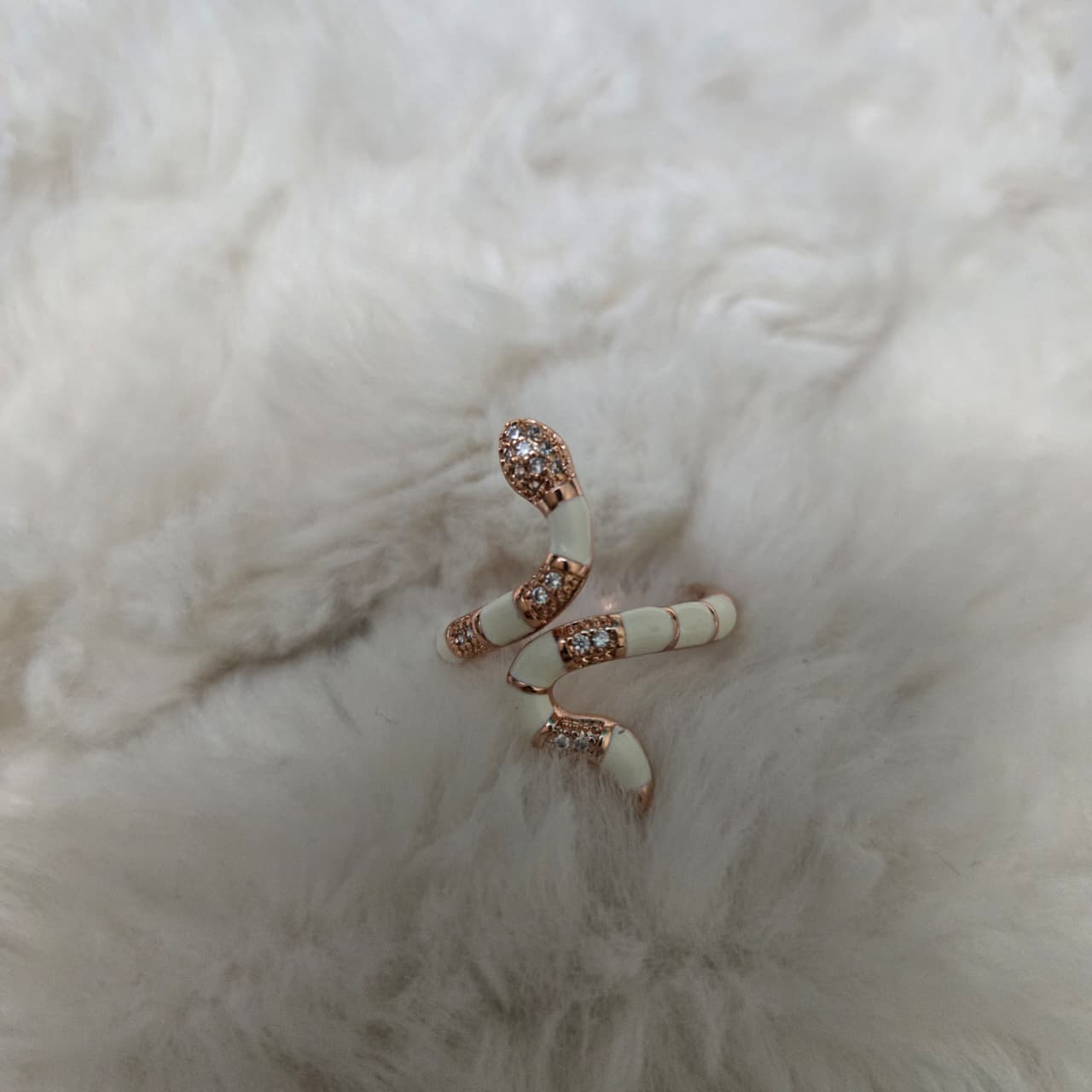 Snake-shaped earring with gemstones on a fluffy white surface