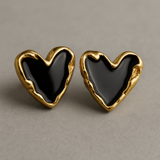 Pair of heart-shaped stud earrings with glossy black enamel centers and textured gold-toned edges, displayed on a neutral background.