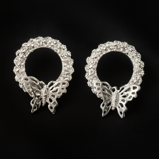 Silver-toned circular stud earrings featuring a textured, beaded design with a detailed butterfly charm at the base.