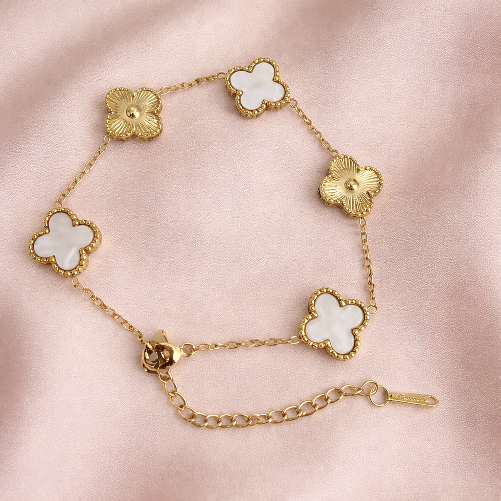 Golden bracelet with textured gold floral motifs and white mother-of-pearl clovers framed with beaded gold edges on a pink cloth.