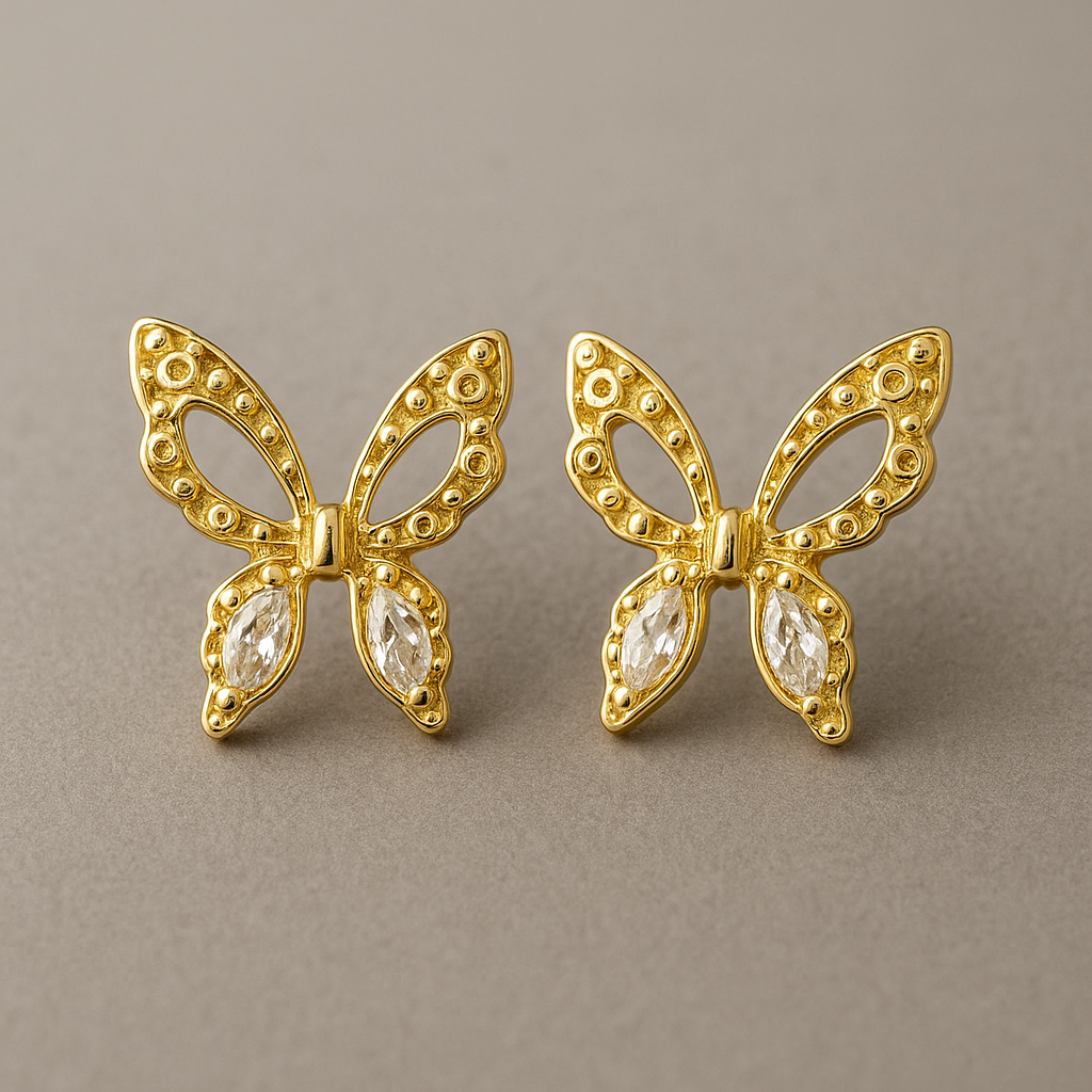 Gold butterfly earrings with gemstones on a brown surface and blurred background
